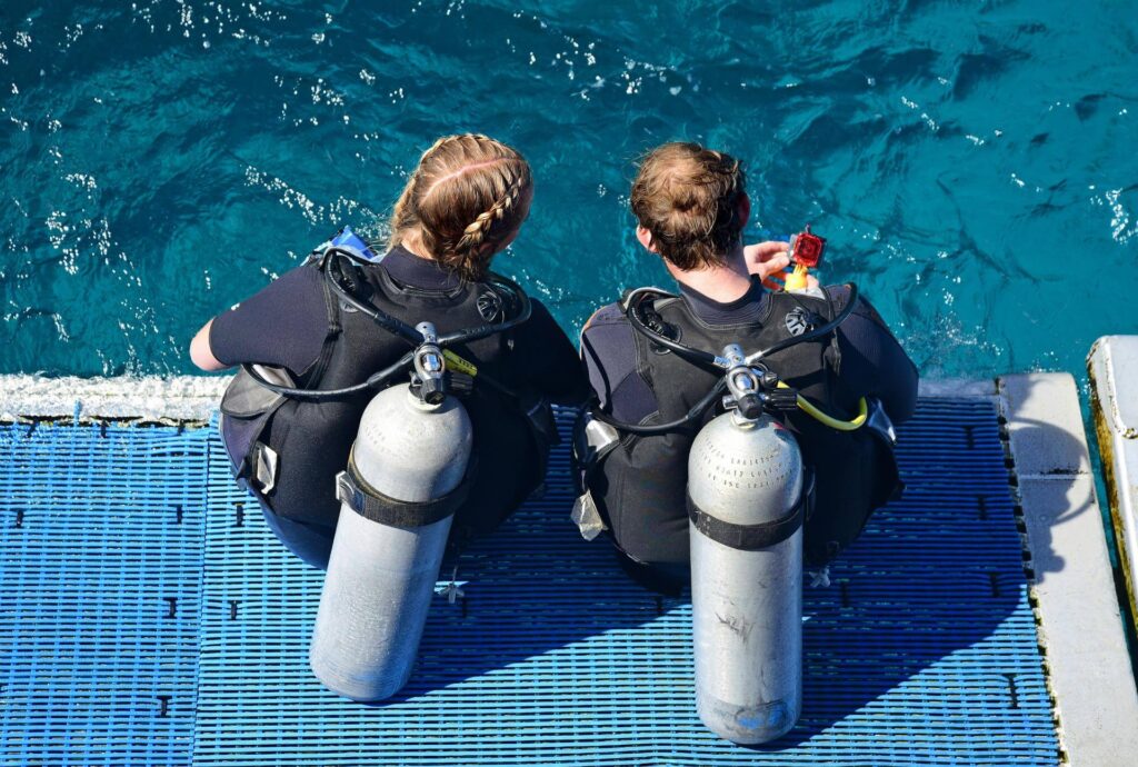 scuba divers sitting with equipment before dive practicing hand signals