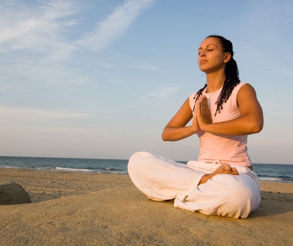 Woman meditating on the beach practicing visualization to reduce dive anxiety and improve buoyancy control.