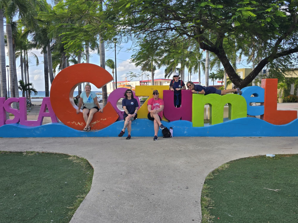 Women scuba divers posing in front of the Cozumel sign during a dive trip