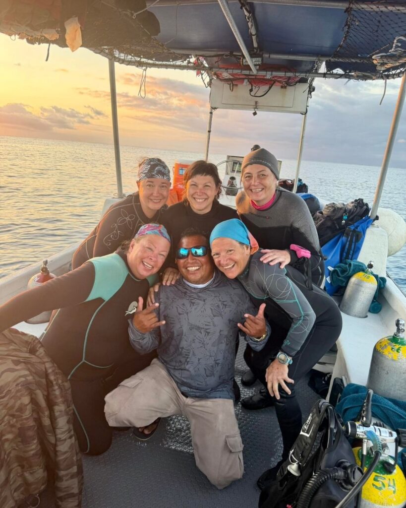 Group of women scuba divers preparing gear on a boat in a supportive environment.
