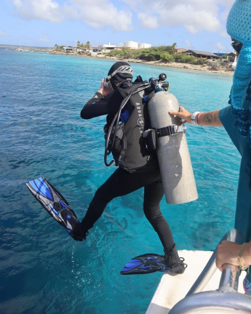 Female scuba diver stepping off a boat platform into calm water in Bonaire