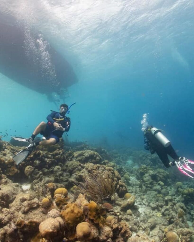 Scuba diver and guide underwater in Bonaire with dive boat visible above