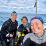 Dive guide assisting two women scuba divers on a boat in a supportive environment in the Philippines