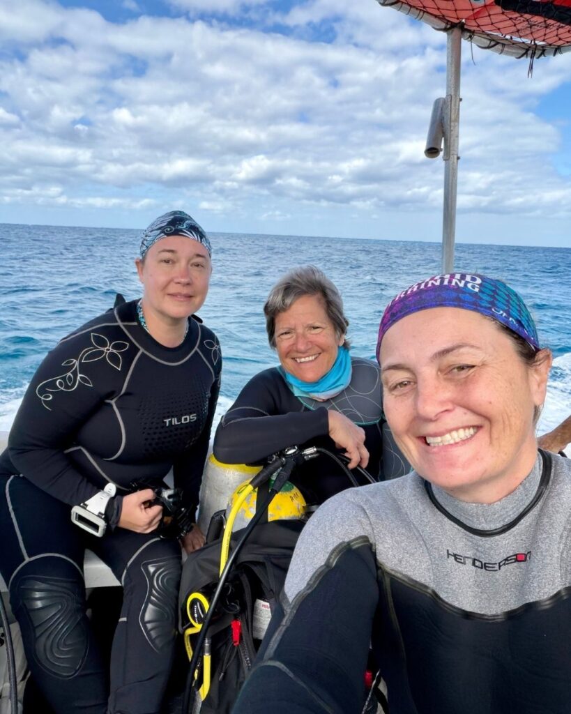 Dive guide assisting two women scuba divers on a boat in a supportive environment in the Philippines