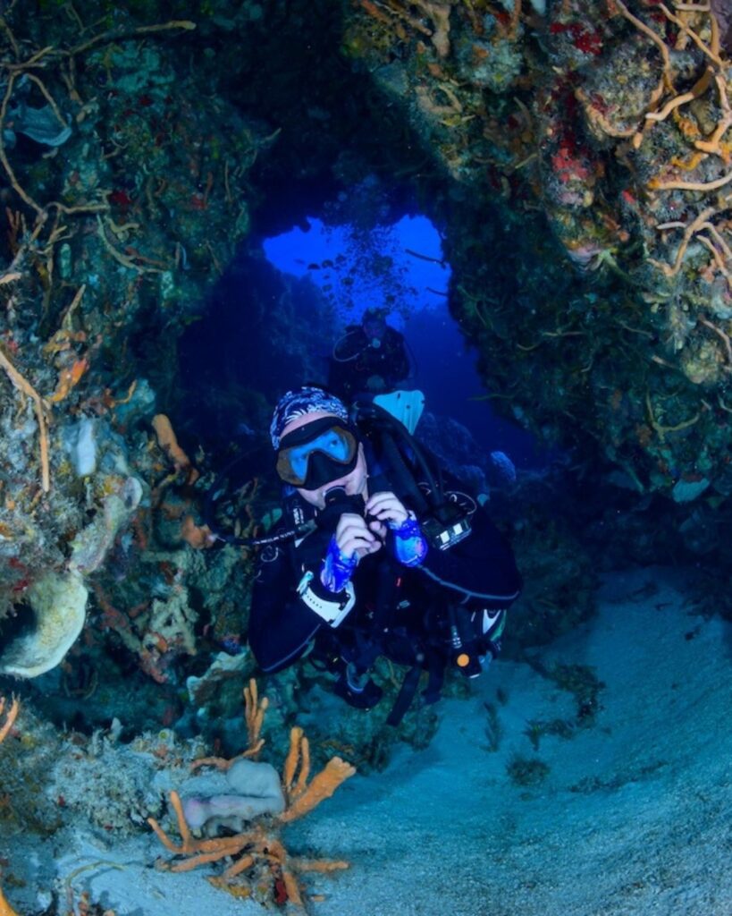 Women scuba divers swimming through a natural cave tunnel in Cozumel reef