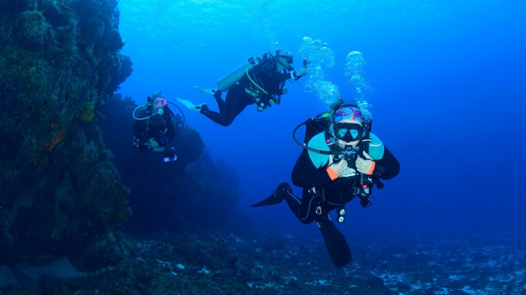 Divers drifting along a coral reef wall at a Cozumel dive site with open blue water