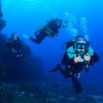 Divers drifting along a coral reef wall at a Cozumel dive site with open blue water