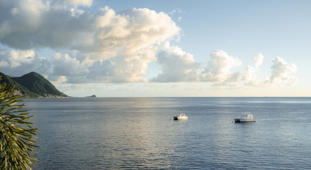 Two dive boats moored on calm blue water off Dominica with the volcanic Scott's Head headland in the background
