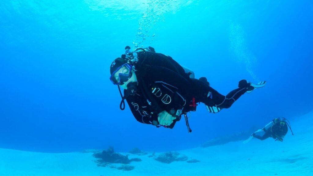 Woman scuba diver hovering calmly in blue water with neutral buoyancy, illustrating somatic practice in scuba diving and nervous system awareness underwater.