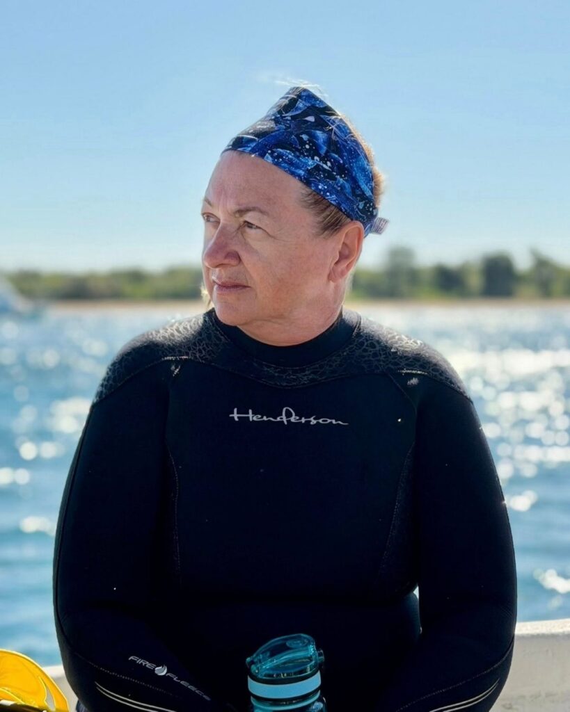 A woman sitting on the back of a dive boat after a dive, wetsuit down to her waist, looking quietly at the water without her phone, warm light around her