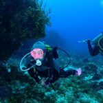 Diver drifting along the Cozumel reef wall with clear blue water and coral formations
