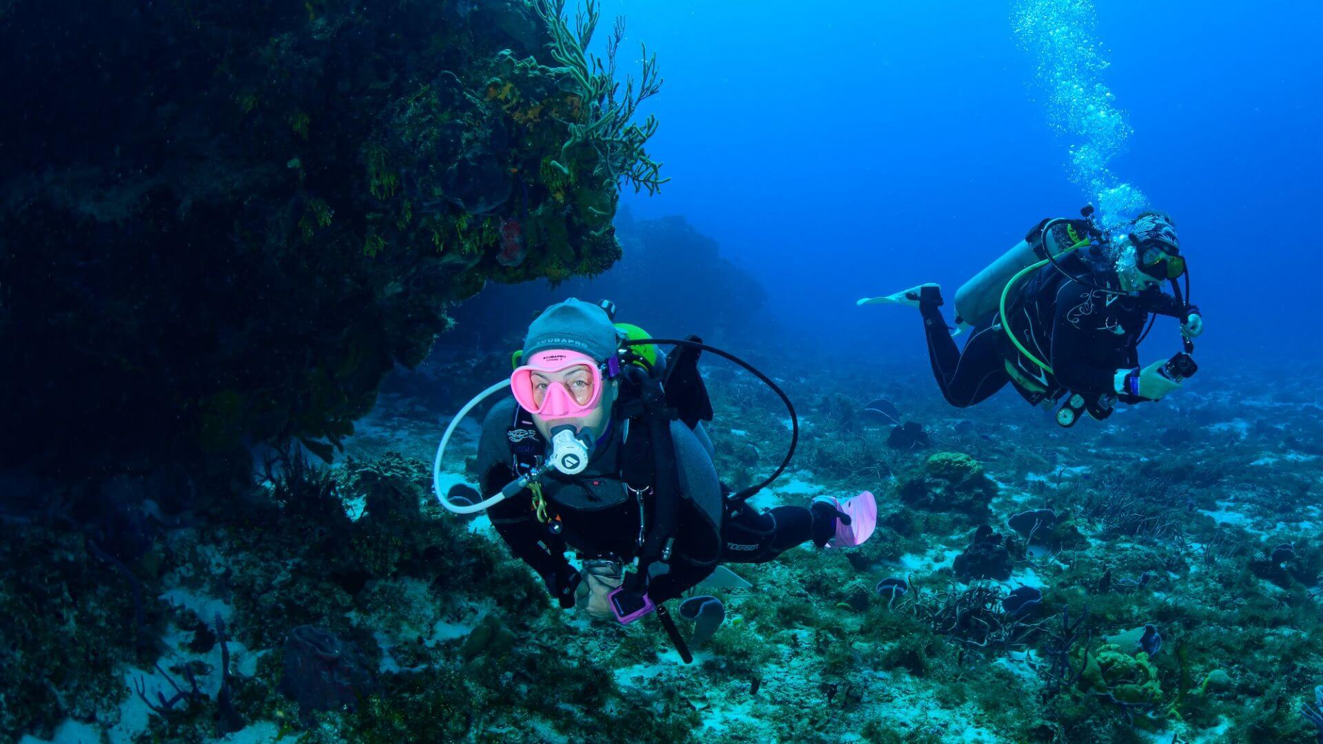 Diver drifting along the Cozumel reef wall with clear blue water and coral formations